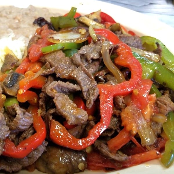 Sizzling beef fajitas with red and green bell peppers, onions, and mushrooms, served with rice and beans.