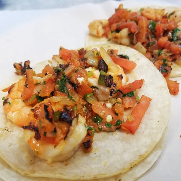 Two shrimp tacos from Taqueria Los Gordos, topped with fresh salsa on white paper.